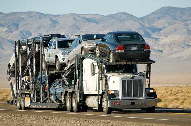 Open car hauler loaded with a pickup truck and sedans crossing a desert highway in West Texas